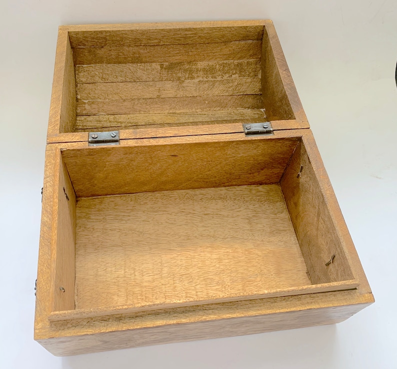 May include: An open, rectangular wooden box with a hinged lid. The box is made of light-coloured wood with visible grain and texture. Metal hinges and small nails secure the lid and box structure. The interior is empty, revealing the box's construction.