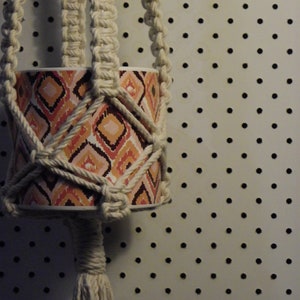 Peut inclure: Un porte-plante en macramé blanc avec un pot à motifs. Le porte-plante est suspendu à un panneau perforé blanc avec des trous noirs.
