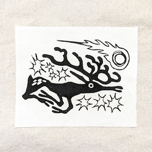 May include: Black and white illustration of a stylized deer running with a comet tail and stars in the background.