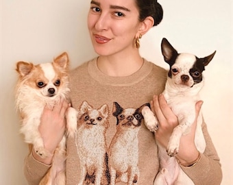 May include: A beige long-sleeve sweater featuring an embroidered graphic of two small dogs on the front. The sweater has a crew neckline and is made of a knit fabric. The design depicts a long-haired dog and a short-haired dog side by side.