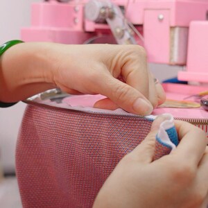 Hands linking the collar of a knitted sweater stitch by stitch on a linking machine dial at our partner workshop