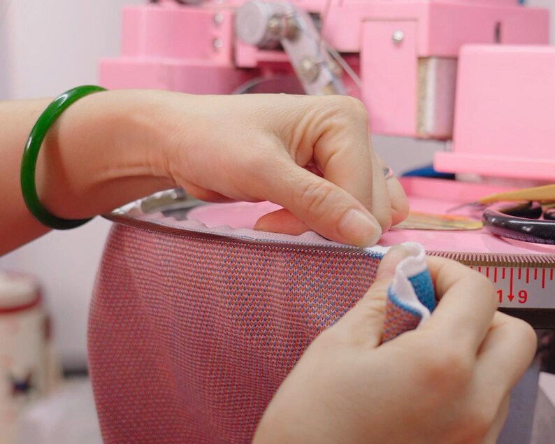 Hands linking the collar of a knitted sweater stitch by stitch on a linking machine dial at our partner workshop