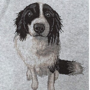 May include: A light gray knit fabric featuring a detailed jacquard-woven graphic of a dog with black and white fur. The dog has a white blaze on its face, dark ears, and a fluffy tail, depicted in a seated position facing forward.