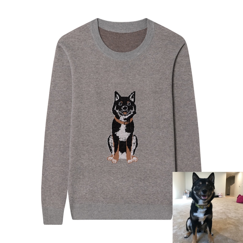 May include: A long-sleeved crew neck sweater in a heathered taupe color. The center of the chest features a knitted graphic of a black and white dog with tan markings, wearing a brown collar, matching the dog shown in the inset photograph.