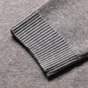 May include: A gray knit sweater sleeve featuring a textured, heathered fabric pattern and a ribbed cuff. The material displays a fine, consistent weave with subtle flecks of darker color throughout the gray base, ending in a structured, elasticized ribbed knit cuff.