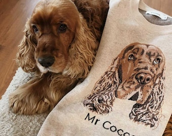 May include: A beige knit sweater featuring a detailed brown and tan cocker spaniel dog portrait graphic on the front. Below the dog illustration, the text Mr Cocco is embroidered in black. The sweater has a crew neckline and ribbed trim.