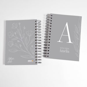 Op de afbeelding: Twee grijze spiraalnotitieblokken met bloemmotieven. Het notitieblok links heeft een bloemmotief en de tekst "Notes from Amelia". Het notitieblok rechts heeft een grote letter "A" en de tekst "Notes from Amelia".