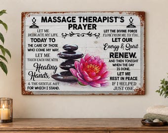 Puede incluir: Un letrero rectangular de metal con un borde oxidado que presenta el texto Massage Therapist's Prayer. El diseño incluye una pila de piedras negras lisas, una flor de loto rosa vibrante y texto negro sobre un fondo de madera blanca.