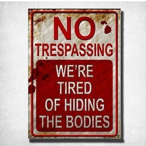 May include: A red and white metal sign with the text "NO TRESPASSING WE'RE TIRED OF HIDING THE BODIES". The sign is distressed and has a rusty appearance.