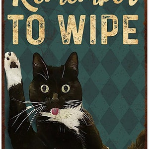 May include: A vintage-style metal sign with a black and white cat licking its nose. The sign has the words "Remember TO WIPE" in gold lettering against a teal diamond pattern background. The sign has a distressed, aged appearance.