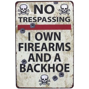 May include: A white metal sign with black text that reads "NO TRESPASSING I OWN FIREARMS AND A BACKHOE". The sign has two skull and crossbones images at the top and bottom, and bullet holes throughout.