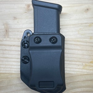 May include: Black plastic magazine holder with a black magazine inside. The holder has two screws on the front and a clip on the side.