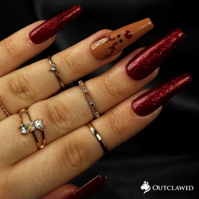 Pode incluir: Unhas compridas de gel vermelho com glitter com uma &uacute;nica unha de destaque com um design de rena marrom.
