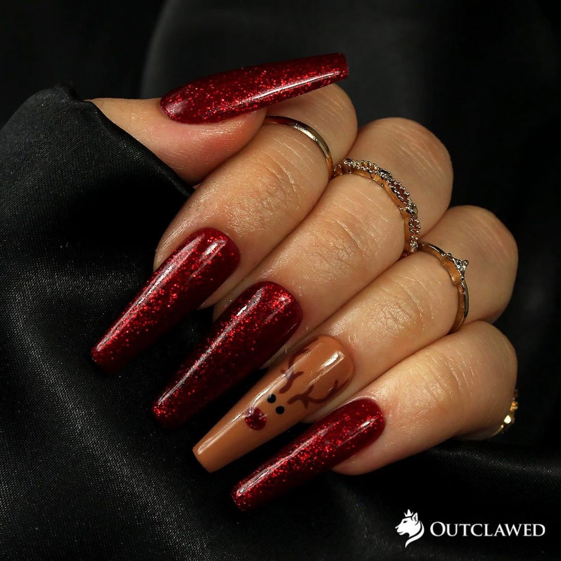 Pode incluir: Unhas compridas de glitter vermelho com uma &uacute;nica unha de destaque com um design de rena marrom.