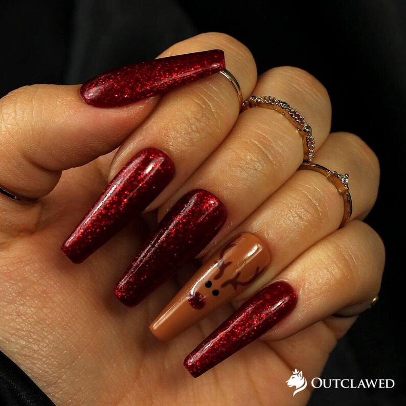 Pode incluir: Unhas compridas de cor vermelha com glitter, com uma &uacute;nica unha de destaque com um design de rena marrom.