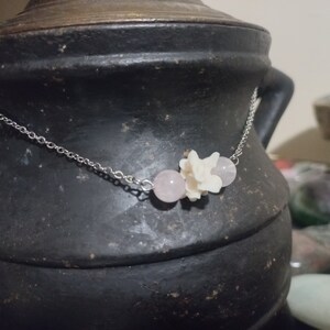 May include: A silver chain necklace with a pink rose quartz bead and a white porcelain flower charm.