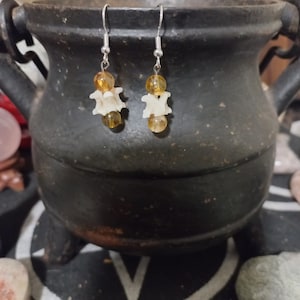 May include: A pair of earrings with a bone charm and amber beads. The earrings are silver and have a hook closure.