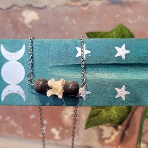 May include: A silver chain necklace with three beads. The center bead is white and the two outer beads are black.