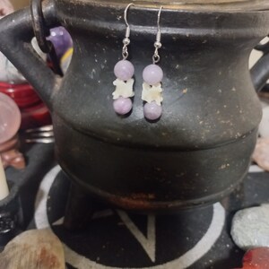 May include: A pair of earrings with purple and white beads. The earrings are made with silver hooks and have a delicate design.