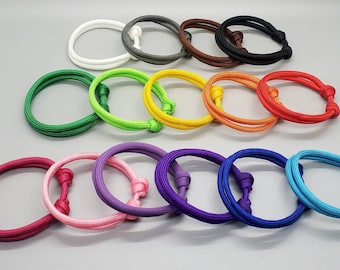 May include: A collection of 14 colorful paracord bracelets with adjustable knots. The bracelets are made of braided rope and come in a variety of colors, including red, orange, yellow, green, blue, purple, pink, and white.