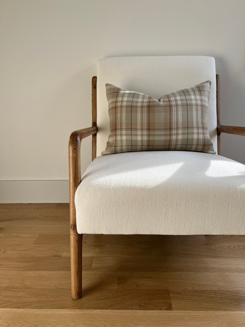 May include: A white armchair with wooden legs and a brown and beige plaid cushion. The chair is sitting on a wooden floor.