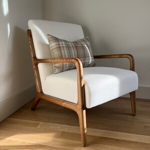 May include: A white armchair with wooden arms and legs. The chair has a brown and beige plaid cushion on it. The chair is sitting on a wooden floor.