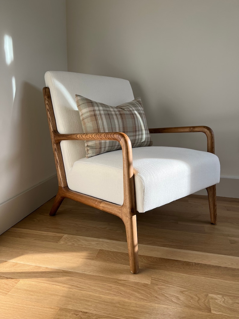 May include: A white armchair with wooden arms and legs. The chair has a brown and beige plaid cushion on it. The chair is sitting on a wooden floor.