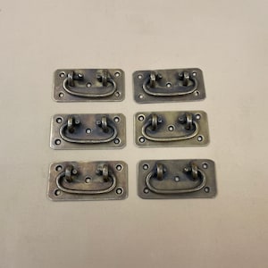 May include: Six antique brass drawer pulls with a rounded rectangular shape and a simple, curved handle.