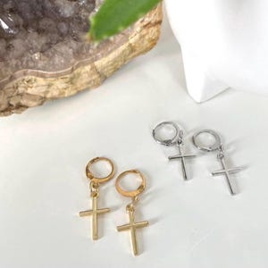 May include: Two pairs of hoop earrings with a dangling cross charm. One pair is gold and the other is silver.