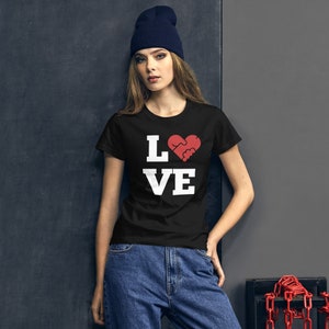Puede incluir: Una camiseta negra con texto blanco que dice "LOVE" con un coraz&oacute;n rojo que presenta dos manos entrelazadas en el centro.