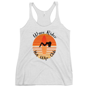 May include: A light gray racerback tank top with a graphic. The graphic features a silhouette of a person on a surfboard, set against an orange and yellow sunset design. Text reads "Wave Rider Hot Wife Club."