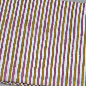 May include: Close-up of a fabric with a repeating vertical stripe pattern. The stripes alternate between white, mustard yellow, and a muted pink color. The fabric appears to be folded, with the pattern visible across the surface.