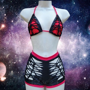May include: Black and red bikini set with a unique cut-out design. The top is a halter style with red lining, and the shorts have a matching red trim. The set is displayed on a mannequin against a space-themed background.