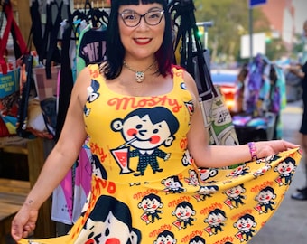 Puede incluir: Un vestido amarillo con un estampado de personajes de dibujos animados bebiendo una bebida. El vestido tiene un escote redondo y es sin mangas. El texto "Mosky" está impreso en el vestido.