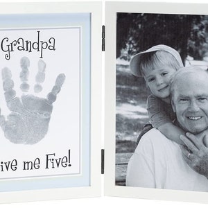 May include: White double picture frame with a black and white photo of a young boy hugging an older man. The other side of the frame has a handprint with the text "Grandpa Give me Five!"