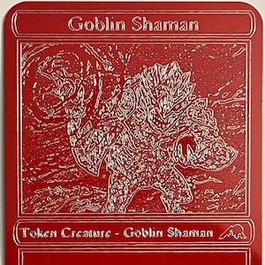 Op de afbeelding: Een rode Magic: The Gathering kaart met een witte rand. De kaart toont een goblin-sjaman-wezen met de tekst "Goblin Shaman" en "Token Creature - Goblin Shaman". De kaarttekst luidt "Whenever this creature attacks, create a Treasure token." De kaart heeft een kracht en uithoudingsvermogen van 2/2.
