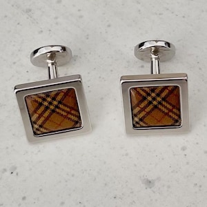 May include: A pair of square cufflinks with a silver-tone frame and a plaid pattern in shades of brown, tan, and black. The cufflinks have a classic design, suitable for formal wear.
