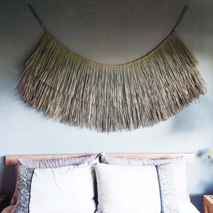 May include: A bedroom with a woven wall hanging above the bed. The bed has a white headboard and white bedding. There are two wicker pendant lights hanging from the ceiling.
