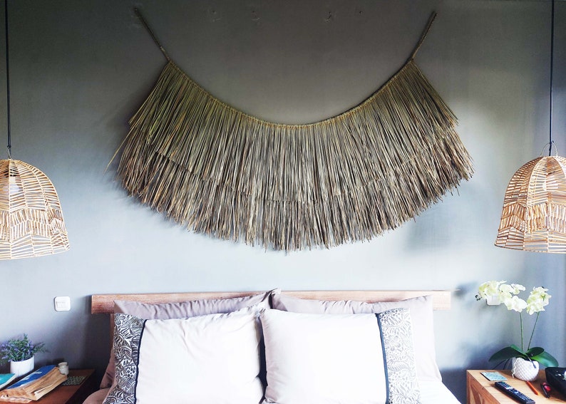 May include: A bedroom with a woven wall hanging above the bed. The bed has a white headboard and white bedding. There are two wicker pendant lights hanging from the ceiling.