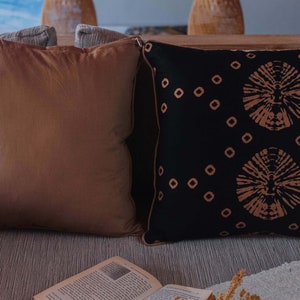May include: Two decorative throw pillows on a couch. One pillow is brown and the other is black with a geometric pattern in a light brown color.