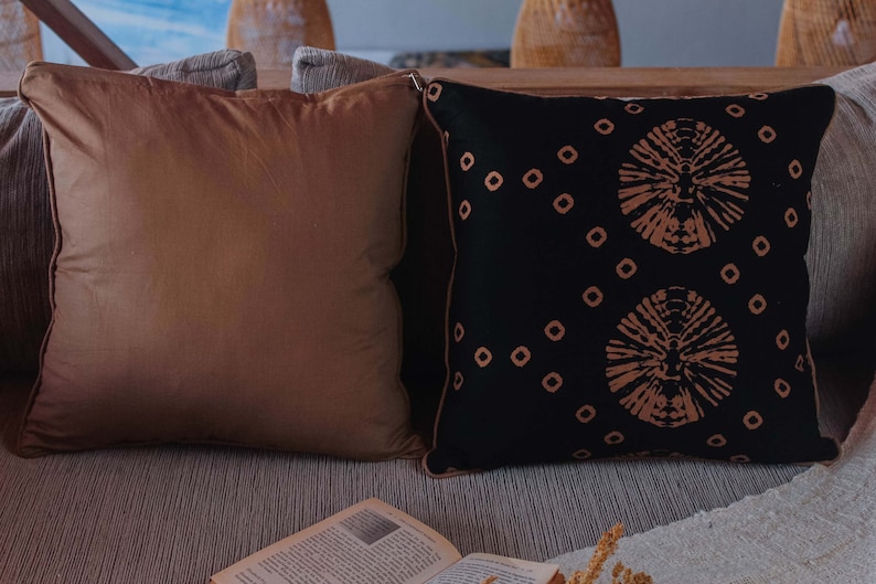 May include: Two decorative throw pillows on a couch. One pillow is brown and the other is black with a geometric pattern in a light brown color.