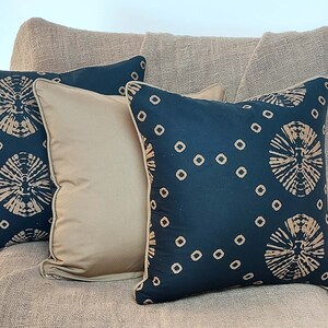 May include: Four throw pillows with a black background and a brown geometric pattern. The pillows are arranged on a brown textured surface.