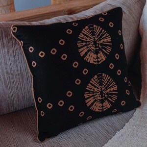 May include: A black throw pillow with a brown geometric pattern. The pillow is sitting on a light brown couch.