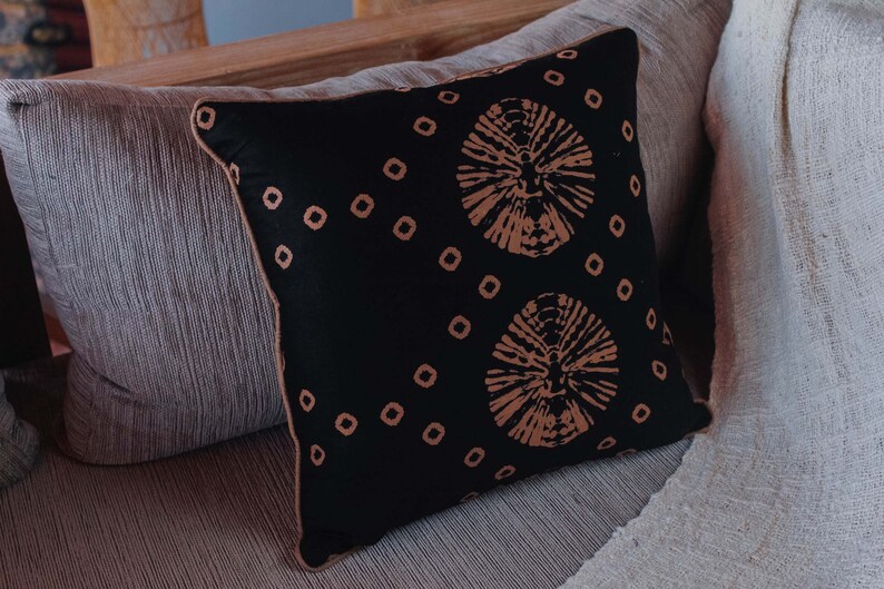 May include: A black throw pillow with a brown geometric pattern. The pillow is sitting on a light brown couch.