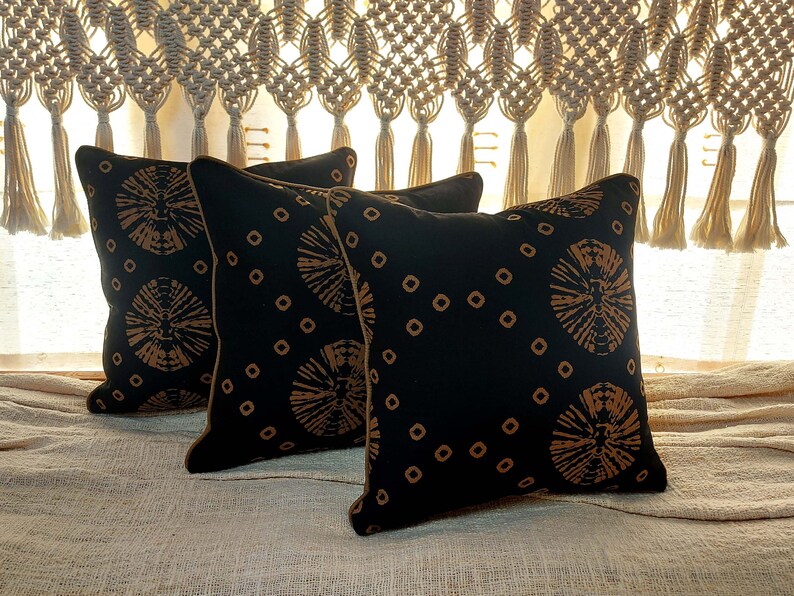 May include: Three black throw pillows with a gold and black geometric pattern. The pillows have a brown trim.