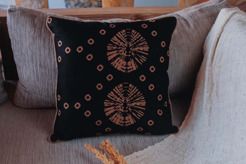 May include: A black throw pillow with a brown and white geometric pattern. The pillow is sitting on a couch with a white throw blanket.