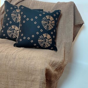 May include: Two black throw pillows with a brown geometric pattern on a brown textured throw blanket.