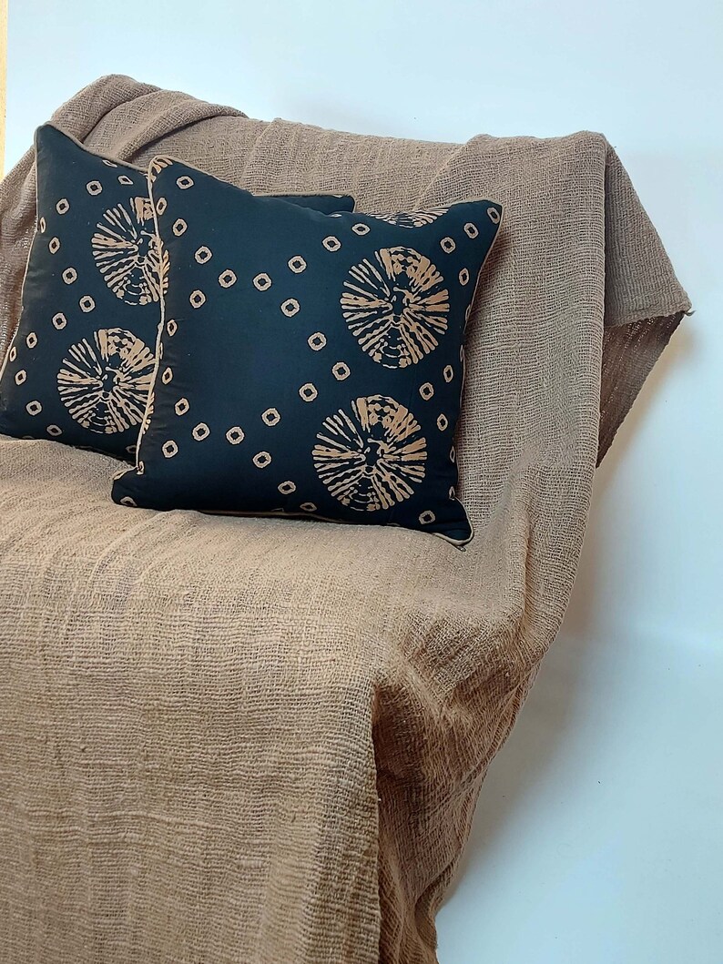 May include: Two black throw pillows with a brown geometric pattern on a brown textured throw blanket.