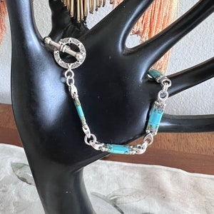 May include: A silver bracelet with turquoise stones and a toggle clasp.