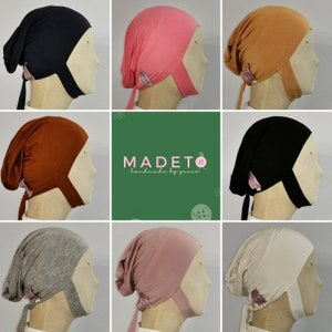May include: Assortment of nine jersey knit head coverings in various colours, including black, pink, brown, grey, and beige. Each head covering has a tie at the back and a small label with the text "MADETO handmade by yunies".